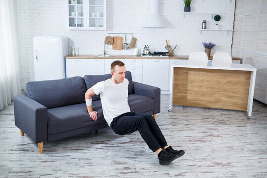 A young man is performing tricep dips as part of his home workout routine in a sleek, modern living room, showcasing his dedication to fitness and wellness through calisthenics and exercise