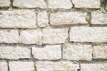 Textured wall of rectangular stone blocks in light beige shades and cement between them.