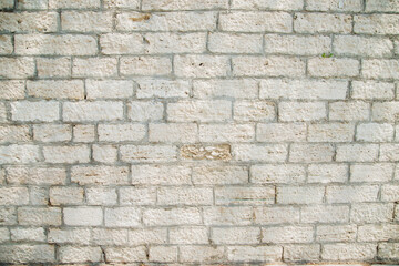 Textured wall of rectangular stone blocks in light beige shades and cement between them.