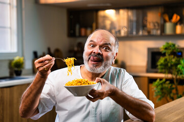 Elderly Indian foodie enjoying noodles in bowl in cozy modern kitchen
