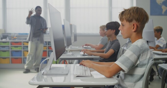 Primary School Students Drawing Pictures on Computers, Working on Creative Projects During Digital Art Class. African American Teacher Educating Diverse Kids. Interactive STEM Learning. Dolly Shot. - Powered by Adobe