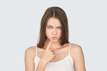 Fototapeta premium Caucasian young female pondering with finger on chin in thoughtful pose on gray background.