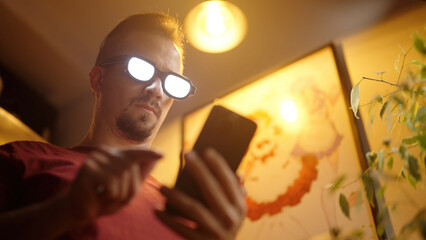 Man with anime glowing glasses swiping on smartphone standing beside a poster with anime maid girls