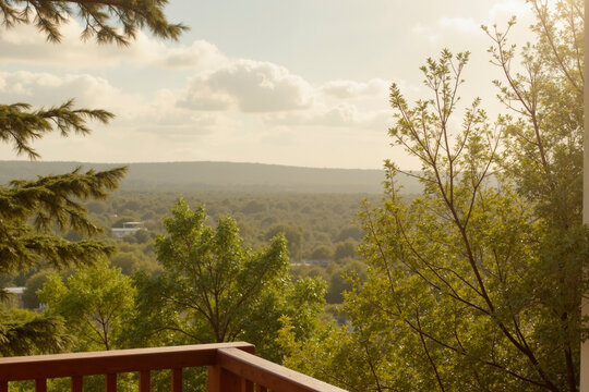 Lush green treetops stretching across rolling hills under partly cloudy sky with wooden balcony railing in foreground, distant landscape fading into horizon, no people visible