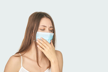 Young caucasian female wearing a mask and coughing against a light background.