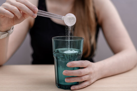 A woman dissolves creatine powder in a glass of water after training.
