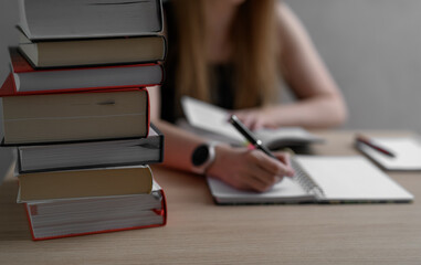 Naklejka premium A woman surrounded by books sits at a desk writing a research paper, essay, or report.