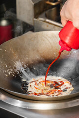 Chef adds sauce to sizzling vegetables in wok during stir-fry cooking. Hot steam rises from creamy mixture. Professional kitchen scene with dynamic culinary action