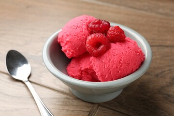 Delicious raspberry sorbet with fresh berries in bowl and spoon on wooden table, closeup