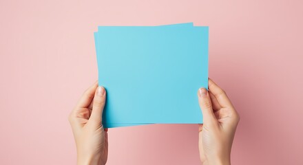 淡いピンク背景の手と空色の紙