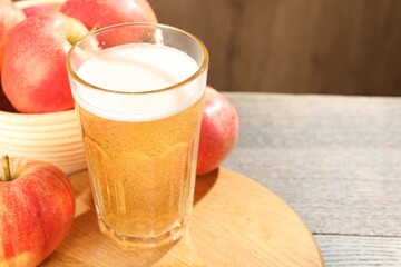 Delicious cider in glass and apples on wooden table, closeup