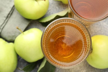 Delicious cider in glasses, apples and leaves on grey textured table, flat lay