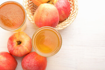 Delicious cider in glasses and red apples on white wooden table, flat lay. Space for text