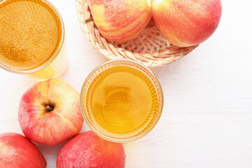 Delicious cider in glasses and red apples on white wooden table, flat lay