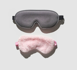 Gray memory foam eye mask and pink fluffy sleep mask on light gray background.