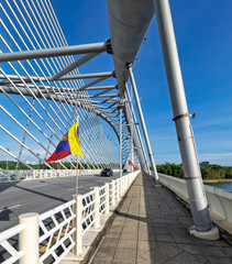 Naklejka premium Seri Wawasan Bridge, Putrajaya, Malaysia. Modern cable-stayed bridge with white cables, road, cars, and pedestrian path under a clear blue sky. Selangor flags visible