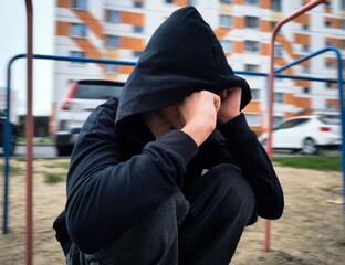 sad lonely teenager. guy in a black hoodie. teenage boy in depression. courtyard of a multi-storey residential building, parked cars, and a teenage boy alone on street © Anastasiya