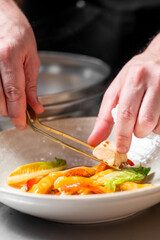 Chef plating gourmet dish with tweezers in professional kitchen. Colorful vegetables arranged with precision. Culinary art, fine dining, and food styling concept