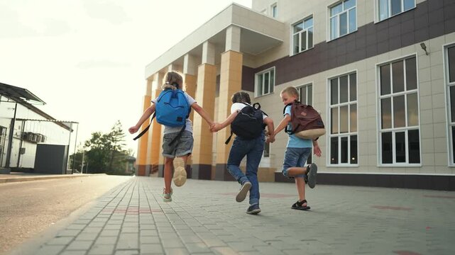Children running toward school building holding hands with backpack and friend, campus walkway and modern facade, summer light, education focus showing childhood energy and safe play. joyful