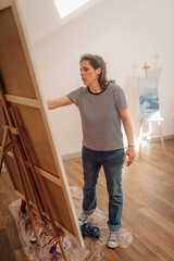 Fototapeta premium Female artist evaluating her painting on canvas in art studio