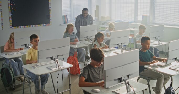 Primary School Students Working on Creative Projects on Computers. African American Teacher Guiding Diverse Kids in Studying Programming During Computer Science Class. Modern STEM Learning. High Angle - Powered by Adobe