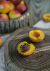Close-up of rustic wooden cutting board with sliced nectarine and bowl of whole nectarines in background. Fresh, organic food preparation and healthy eating concept