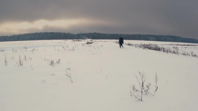 Man Hiking Through Deep Snowy Field with Backpack in Winter Landscape