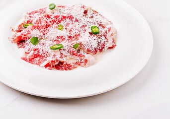 Slices of raw beef with cheese and green peppers served on a white plate