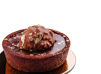 Exquisite chocolate tart topped with a golden praline on a golden plate