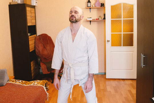 Focused man in white karate gi meditating or practicing martial arts at home. Represents discipline, mindfulness, and a healthy lifestyle. Perfect for wellness, fitness, or personal growth concepts.