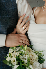The bride and groom are standing side by side, hugging each other, showing off their gold wedding rings and a bouquet of white roses in the bride's hands