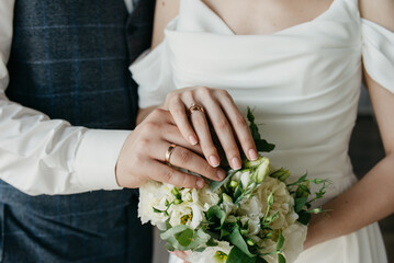 The bride and groom standing side by side, placing their hands with wedding rings on their fingers,...