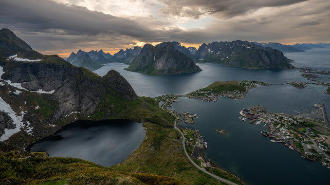 Aerial view of dramatic fjords meet the quaint village, cradled by jagged peaks under a brooding sky, Srvgen, Nordland, Norway.