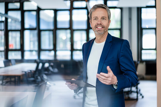 Self-confident businessman in blazer working with tablet in modern office