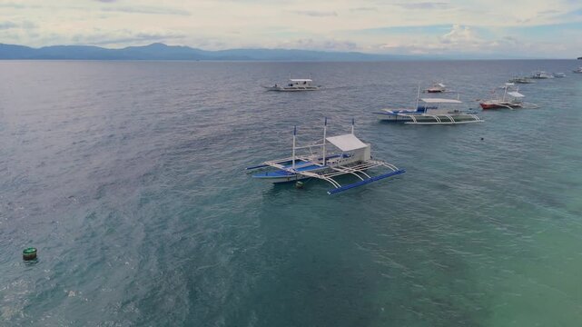Aerial view of several traditional Filipino outrigger boats floating on the clear ocean water near a sandy coastline, Moalboal, Cebu, Philippines.