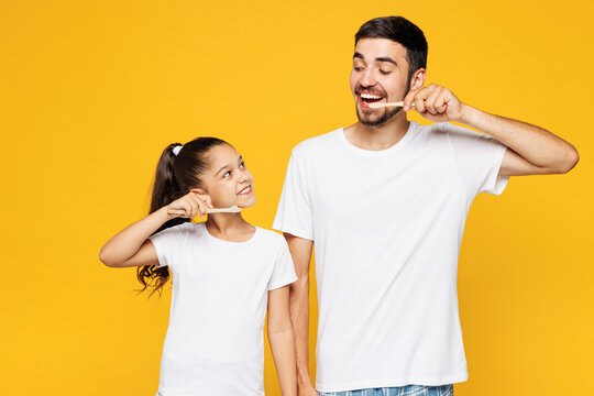 Young happy parent man have fun with child girl wear casual blue pyjamas clothes. Daddy little kid daughter brushing teeth isolated on plain yellow wall background. Father's Day Love family concept. - Powered by Adobe