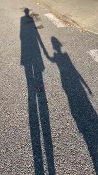 Beautiful shadows of a parent and child holding hands while walking on a sunny road, capturing a moment of love and connection. User generated content