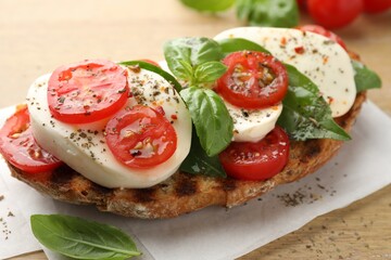 Delicious sandwich with mozzarella cheese, tomatoes and basil on wooden table, closeup