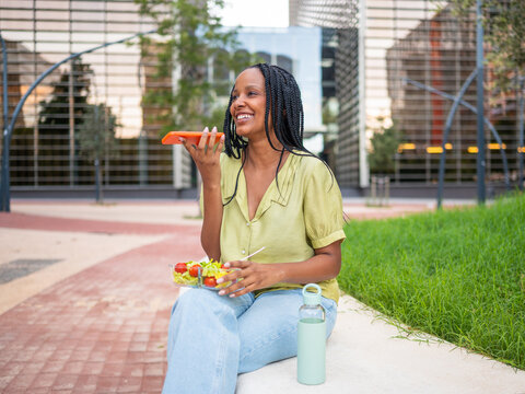 Happy young manager eating salad and using smartphone on lunch break outdoors - Powered by Adobe