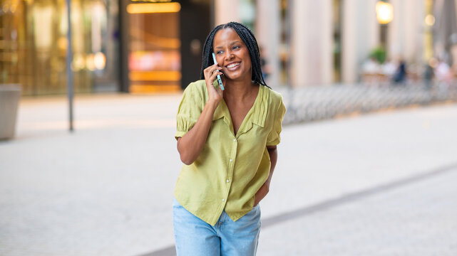 Smiling businesswoman walking and talking on smartphone in urban city - Powered by Adobe