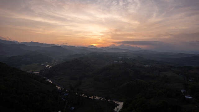 Aerial view of sunlight filtering through the clouds over rolling hills and a winding river, casting long shadows across the landscape, Soppeng, Sulawesi Selatan, Indonesia.