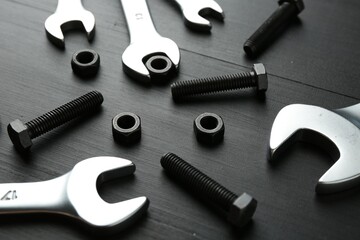 Many metal wrenches, bolts and nuts on black wooden table, closeup