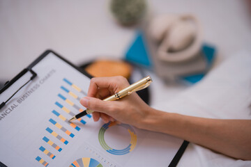 Businesswoman is analyzing financial business charts using pen, working from home or office, with some cookies and headphones in the background