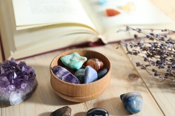 Different healing stones, book and lavender on wooden table, closeup