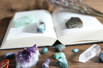 Different healing stones and book on wooden table, closeup