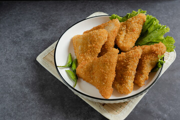 Risol Mayo segitiga or Triangle Risol mayonnaise served in a white bowl with fresh lettuce and green chili on dark background. Showcasing a savory Indonesian snack with breadcrumb coating. 