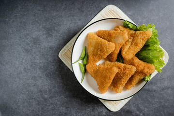 Top view Risol Mayo segitiga or Triangle Risol mayonnaise served in a white bowl with fresh lettuce and green chili on dark background. Showcasing a savory Indonesian snack with breadcrumb coating. 