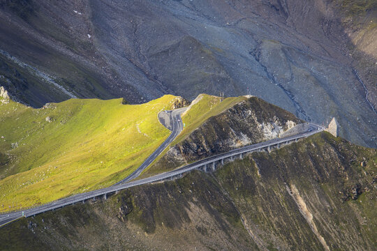 Aerial view of a winding road slicing through the rugged, sun-kissed landscape of Grossglockner High Alpine Road, Fuscher T&Atilde;&para;rl, Bruck an der Gro&Atilde;&Yuml;glocknerstra&Atilde;&Yuml;e, Salzburg, Austria.