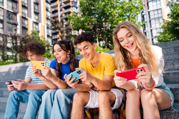 Group of cheerful young friends enjoying a sunny day, engaging with smartphones on urban outdoor steps