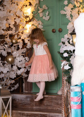 A girl in an elegant pink dress walks down the steps near a tree decorated with toys.